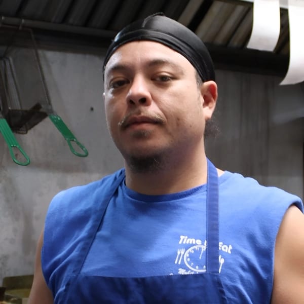 A Time To Eat Cafe employee in a blue shirt and black durag looks directly at the camera.