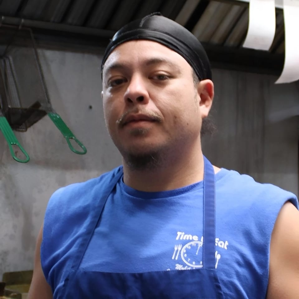 A Time To Eat Cafe employee in a blue shirt and black durag looks directly at the camera.