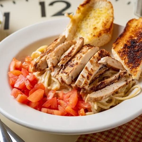 Grilled chicken pasta with diced tomatoes and garlic bread on a white plate at Time To Eat Cafe.