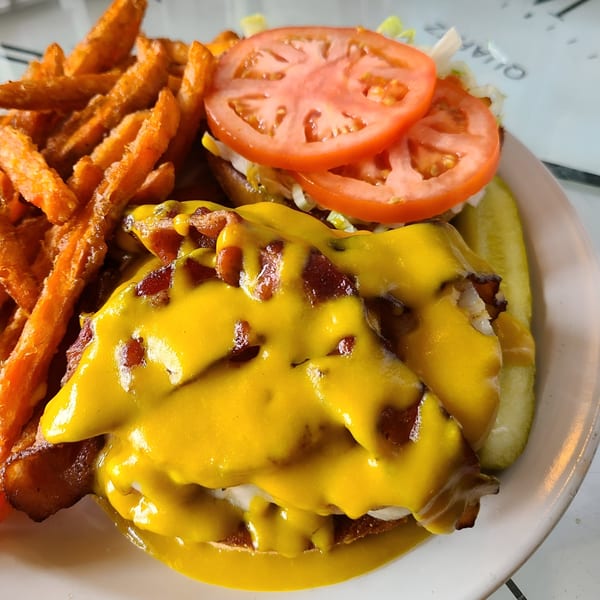 A bacon cheeseburger with melted cheese, lettuce, tomato, and a side of sweet potato fries.