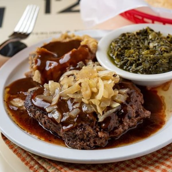 Salisbury steak with gravy and onions, mashed potatoes, and a side of collard greens.